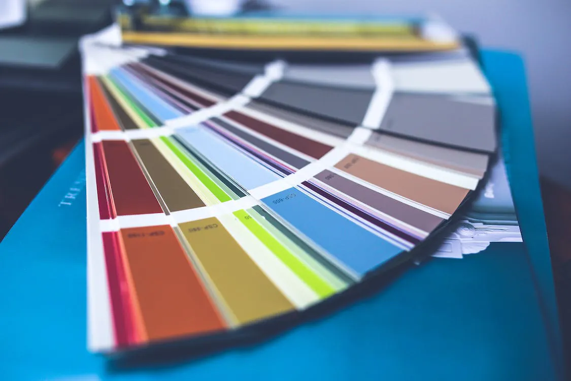 A fanned-out set of color swatches displaying a variety of colors, arranged in a gradient from warm shades to cool tones, placed on a blue surface.