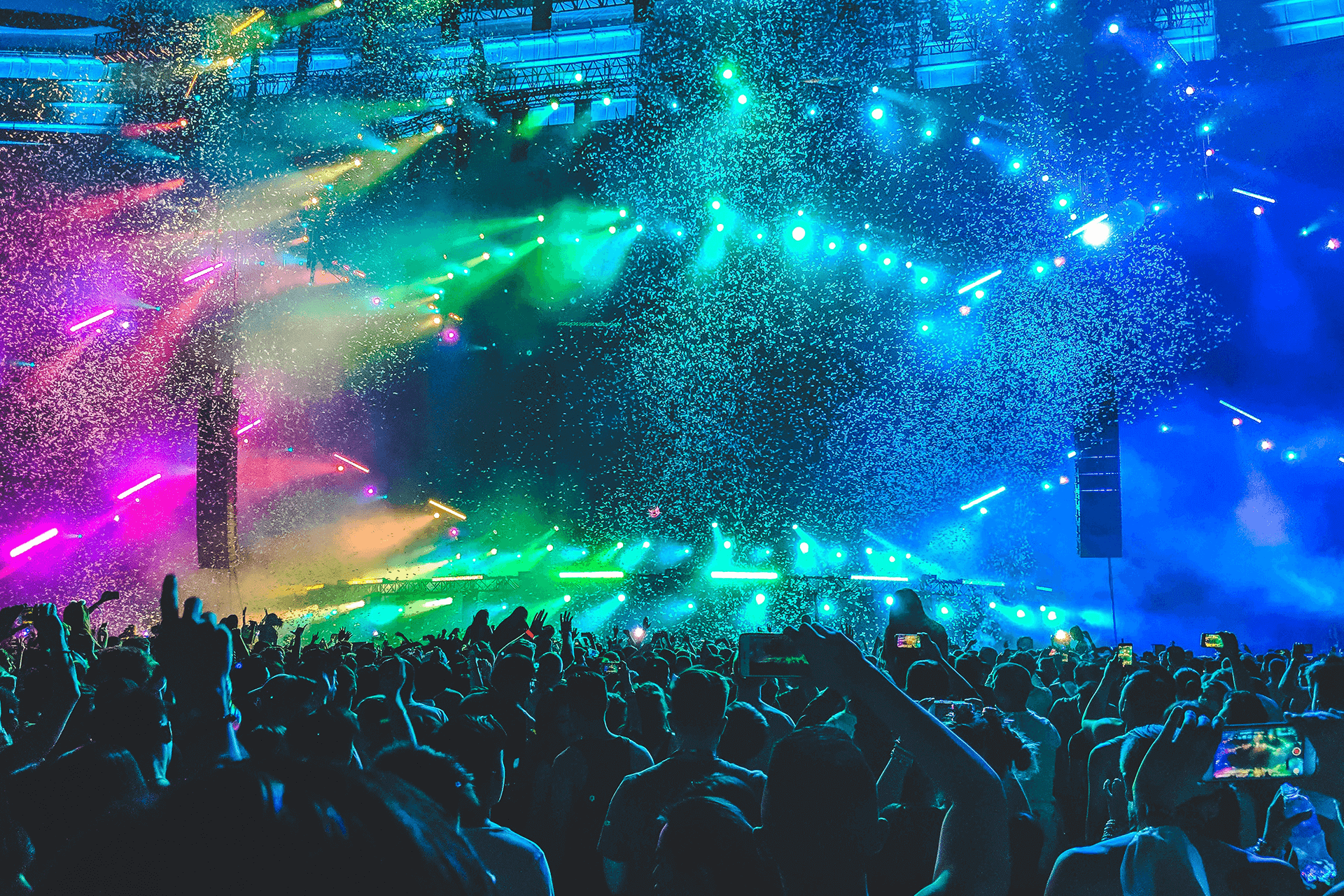 A crowd of people at a concert with colorful lights and confetti in the air.