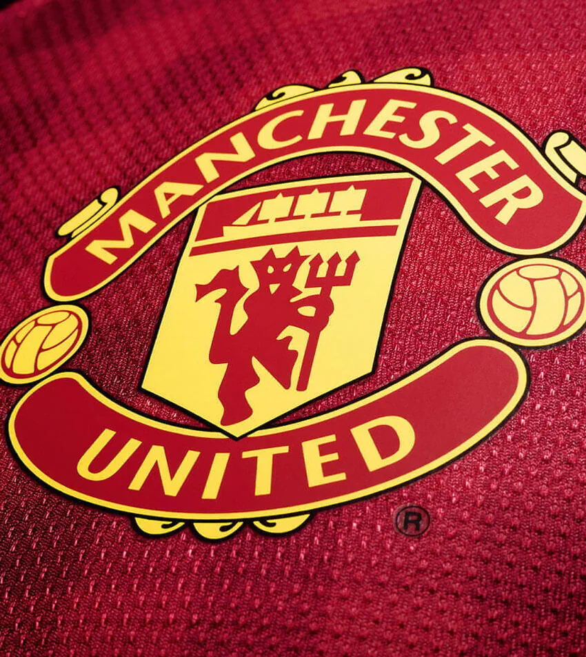 Manchester United football club logo in red and yellow on a red fabric background.