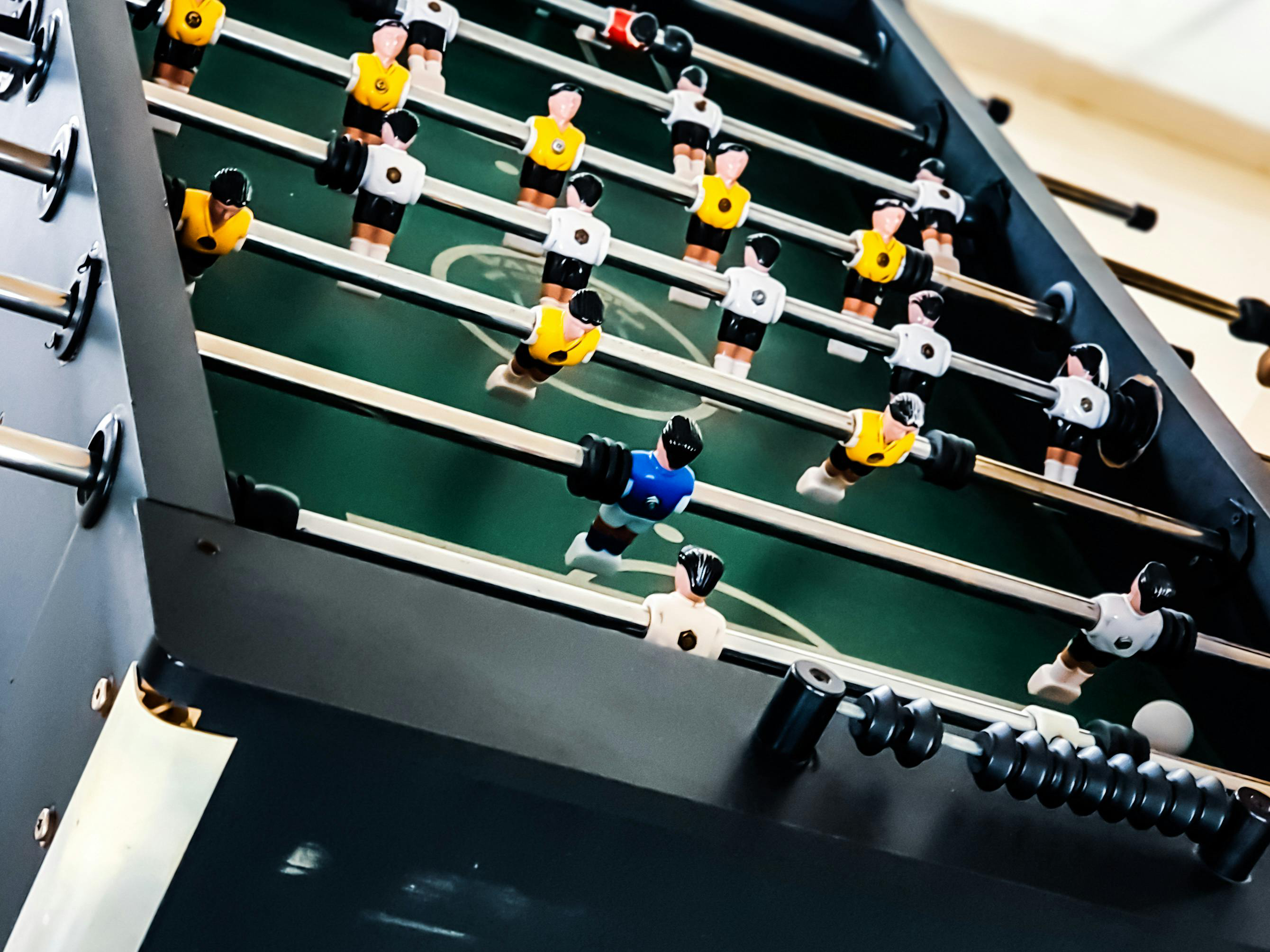 Close-up of a foosball table with plastic soccer player figures on metal rods, painted in yellow, white, and blue outfits.