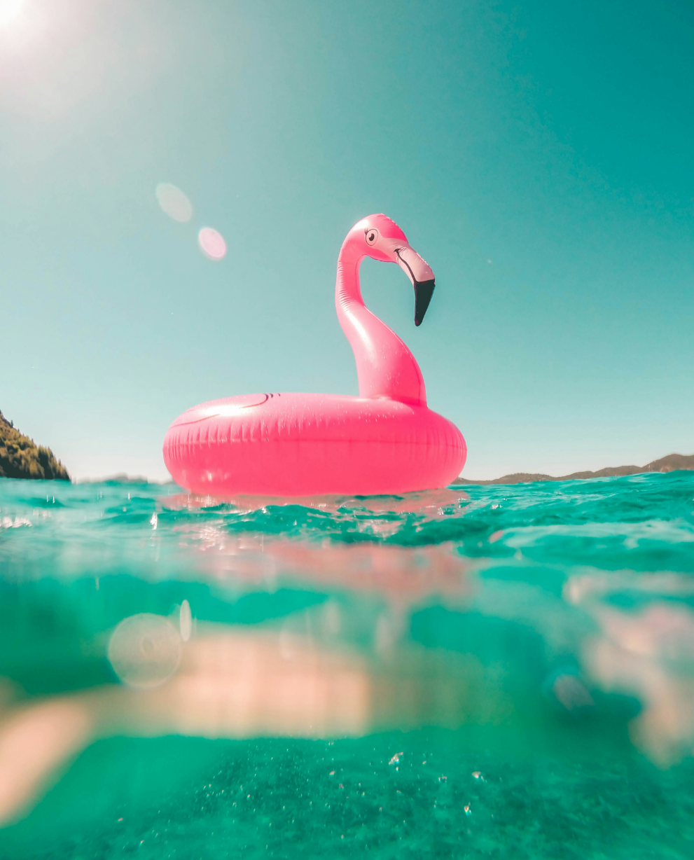 A bright pink flamingo-shaped inflatable float on turquoise water, under a clear sky.