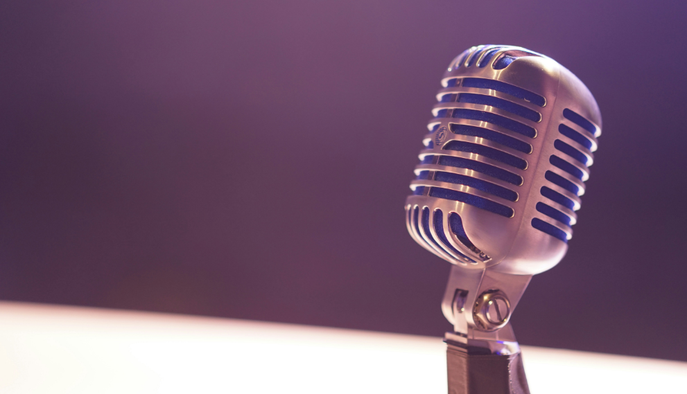 Close-up of a vintage-style microphone with a metallic finish, set against a blurred purple and white background.