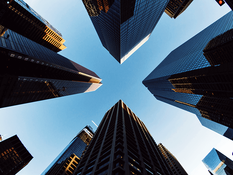 Upward view of tall skyscrapers forming a circular arrangement, set against a clear blue sky.