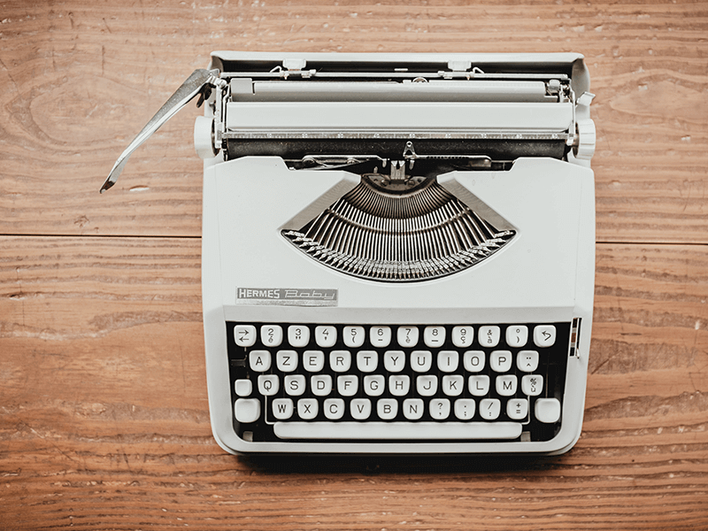 A vintage white Hermes Baby typewriter sits on a wooden surface, displaying qwerty keys and a paper roller—an echo of the timeless relevance of quality content.