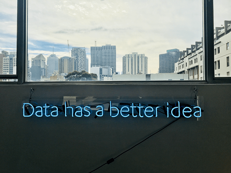 Neon sign reading "Data has a better idea" mounted on a wall with a window overlooking city buildings in the background.