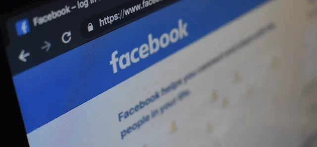 Close-up of a computer screen displaying the Facebook login page. The Facebook logo is prominent at the top in white text on a blue background.